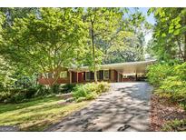 Charming brick home with a red front door and a covered carport surrounded by lush greenery at 3571 Lake Se Dr, Smyrna, GA 30082