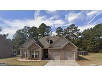 Charming brick home featuring an attached two-car garage, manicured lawn and a welcoming front entrance and stone patio at 1128 Carillon Se Dr, Conyers, GA 30013