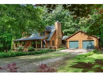 Charming log home with a covered front porch and an attached two-car garage, surrounded by lush greenery and mature trees at 6605 Old White Mill Rd, Fairburn, GA 30213
