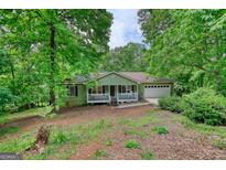 Charming single-story home featuring a quaint front porch and a two-car attached garage nestled among mature trees at 1638 River Trc, Auburn, GA 30011