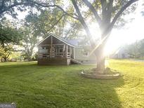 Charming cottage with a covered front porch, mature trees, and a spacious lawn bathed in golden sunlight at 316 Gaithers Rd, Mansfield, GA 30055