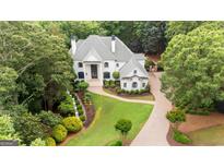 Stately white home with professionally landscaped yard and brick driveway, surrounded by mature trees at 8957 Old Southwick Pass, Johns Creek, GA 30022