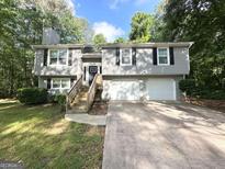 Split-level home featuring a two-car garage, wood staircase, black shutters, and gray siding at 5405 Lakeside Dr, Union City, GA 30291