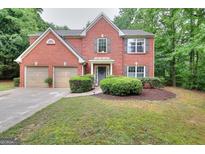 Charming two-story red brick home featuring a manicured lawn and a two-car garage, nestled among mature trees at 5765 Woodstone Dr, Cumming, GA 30028
