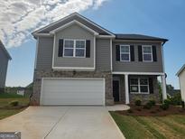 Charming two-story home featuring a two-car garage, gray siding and brick accents, complemented by a well-manicured lawn at 609 Lobelia Way, Locust Grove, GA 30248