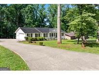 Charming single-story home featuring a long driveway, white brick, dark shutters, and lush landscaping at 3210 Roseheath Ln, Lithonia, GA 30038