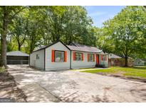 Charming single-story home features a concrete driveway, gray siding, and vibrant orange window shutters at 5180 Ash St, Forest Park, GA 30297