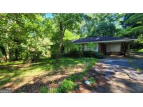 Ranch style home with brick exterior and carport surrounded by mature trees and an overgrown lawn at 1417 Lake Cir, Mableton, GA 30126