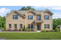 Charming two-story brick home with landscaped yard, complemented by dark shutters and a welcoming front entrance at 361 Traditions Lane, Hampton, GA 30228