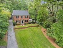 Charming two-story brick home with manicured lawn, brick retaining wall, and mature trees, nestled in a lush, green landscape at 905 Stovall Ne Blvd, Atlanta, GA 30319