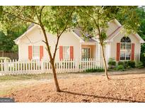Charming home featuring a white picket fence, complemented by trees and light-colored siding with red shutters at 110 Orchard Vw, Fayetteville, GA 30215