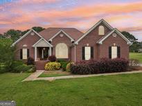 Charming brick home with manicured lawn and colorful landscaping, set against a vibrant sunset sky at 1535 Lake Dow Rd, Mcdonough, GA 30252