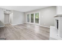 Bright living room with white fireplace, new gray floors, and access to the outdoor patio at 113 Tuxworth Cir, Decatur, GA 30033