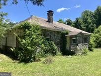 Exterior view of a stone-clad home with an overgrown yard needing landscaping and repair at 72 N Pomona N Rd, Hampton, GA 30228
