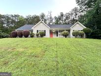 Charming ranch-style home featuring a well-manicured lawn, gray siding, black shutters, and a welcoming red front door at 9124 Comstock Ct, Covington, GA 30014