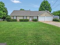 Charming single-story home featuring a manicured lawn, trimmed hedges, and a two-car garage at 130 Belmont Trl, Covington, GA 30016
