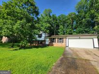 Charming two-story home with brick accents, attached garage, and a lush green lawn surrounded by mature trees at 7290 Grayson Dr, Riverdale, GA 30296