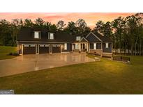 Beautiful exterior of home with large driveway and three-car garage, with a colorful sunset in the background at 180 Lapis Lake Pt, Fayetteville, GA 30215