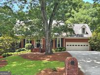 Traditional red brick home featuring a manicured lawn and a two-car garage nestled among mature trees at 2010 Pearwood Path, Roswell, GA 30076