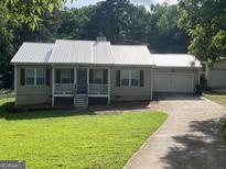 Charming single-story home with a metal roof, a front porch, an attached garage, and a driveway at 5761 Hancock Dr, Social Circle, GA 30025