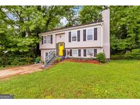 Charming split-level home featuring a bright yellow door, black shutters, and lush green landscaping at 4651 Garden Hills Dr, Stone Mountain, GA 30083