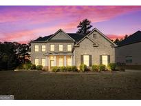 Charming two-story brick home with well-manicured lawn and inviting front porch, with warm-lit windows at 6857 Louis Dr, Locust Grove, GA 30248
