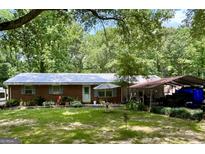 Charming single-story home with a brick facade, metal roof, and a spacious, green lawn and mature trees at 3683 Miller St, Lithia Springs, GA 30122