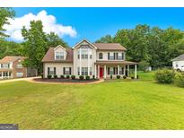Charming two-story home with a manicured lawn and a welcoming front porch and a bright red front door at 355 Sturgess Run, Sharpsburg, GA 30277