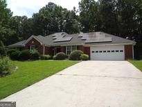 Charming red brick home featuring a paved driveway, two-car garage, solar panels, and lush front lawn at 2958 Mary Alice Trl, Loganville, GA 30052