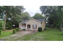 Charming single-story home with a well-maintained lawn, complemented by mature trees, beige siding, and a cozy front porch at 1581 Jersey Social Circle Rd, Covington, GA 30014