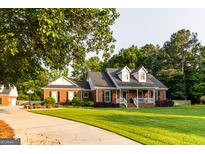 Charming brick home featuring a covered front porch and lush green lawn with mature trees at 30 Carolyn Ct, Social Circle, GA 30025