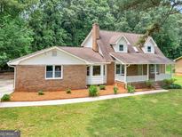 Charming brick home featuring a well-manicured lawn, mature trees, and a welcoming front porch at 90 Country Roads Cir, Stockbridge, GA 30281