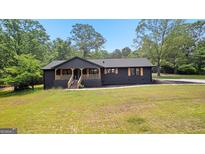 Charming black home with a covered front porch and natural wood accents surrounded by lush greenery at 8129 S Giles Rd, Douglasville, GA 30135