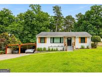 Charming single-story white home with a green lawn, carport, and natural wood accents on windows and front door at 1981 Shalimar Ne Dr, Atlanta, GA 30345