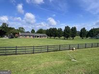 Sprawling front yard with a charming ranch-style home and a classic black wooden fence enhancing the curb appeal at 12621 Highway 142, Oxford, GA 30054