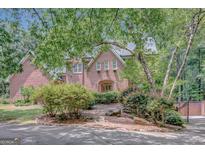 Charming brick home featuring an arched entrance, lush landscaping, and mature trees providing shade and privacy at 305 Sherwood Rd, Fayetteville, GA 30215