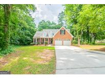 Charming brick home with a two-car garage and a long driveway surrounded by mature trees and a lush lawn at 70 Sylvia Cir, Covington, GA 30016