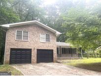 Brick home featuring a two-car garage and a welcoming covered porch, surrounded by mature trees at 345 Fond Du Lac Dr, Stone Mountain, GA 30088