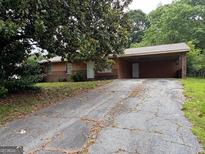 Ranch home featuring a covered carport, front yard with mature trees and a long driveway at 1932 Pharrs Rd, Snellville, GA 30078