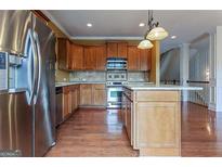 Bright kitchen with hardwood floors, stainless steel refrigerator, kitchen island, and natural wood cabinetry at 275 Autry Mill Ln, Suwanee, GA 30024