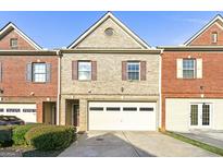 Inviting townhome showcasing a brick and tan facade, a front-entry garage, and manicured landscaping at 7177 Fringe Flower Dr, Austell, GA 30168