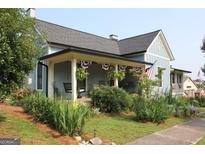 Charming home featuring a welcoming covered porch decorated with patriotic bunting and lush landscaping at 5880 Mulberry St, Austell, GA 30168