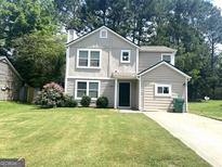Charming two-story home featuring light beige paint, a well-manicured lawn, and beautiful landscaping at 6300 Creekford Ln, Lithonia, GA 30058
