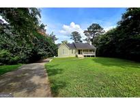Charming single-story home featuring a welcoming front porch and surrounded by lush greenery on a sunny day at 165 Cedar Ridge Rd, Locust Grove, GA 30248