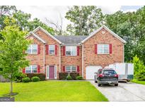 Beautiful two-story brick home featuring red shutters, a well-manicured lawn, and mature trees at 1849 Wanda Way, Ellenwood, GA 30294