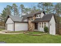 Charming home featuring stone accents, a two-car garage, a lush lawn, and mature trees in a serene setting at 5368 Nw Stafford Nw Dr, Lilburn, GA 30047