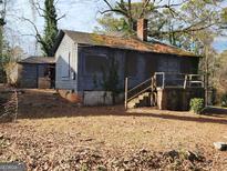 Shot of a rundown two story house with faded gray siding and covered windows at 366 Seventh Ave, Scottdale, GA 30079