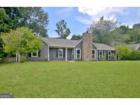 Charming single-story home with a stone chimney, complemented by a lush green lawn and mature trees at 110 Chesterfield Ct, Fayetteville, GA 30214