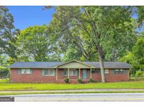 Charming one-story brick home featuring mature trees and traditional curb appeal with green shutters on the windows at 1189 E Fayetteville Rd, Riverdale, GA 30296