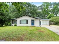 Charming single-story home with a white brick exterior, blue door, and a well-manicured front lawn surrounded by mature trees at 1694 Pheasant Dr, Atlanta, GA 30238